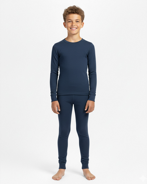 A boy wearing a denim-blue long-sleeve Merino wool base layer top and matching leggings, standing barefoot in a white studio.