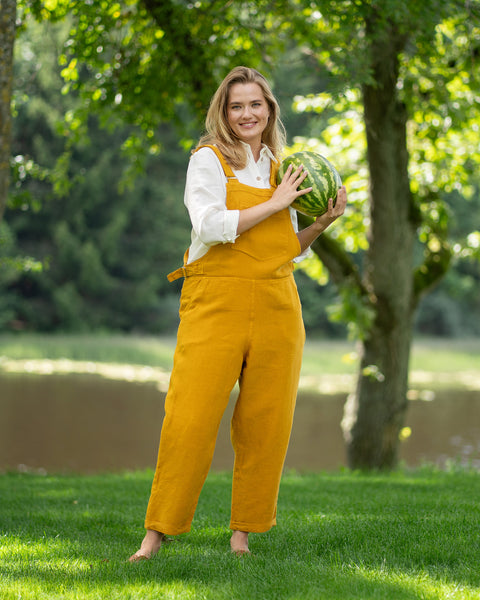 Woman in yellow Nicci linen jumpsuit holding a watermelon slice in a park like setting