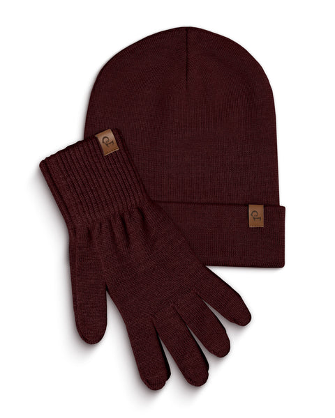 A royal cherry knitted beanie and a pair of matching gloves are laid flat against a white background. Both the beanie and each glove have a small, rectangular brown leather tag with a menique logo on them. The items are slightly overlapping, with the beanie positioned above and to the left of the gloves.