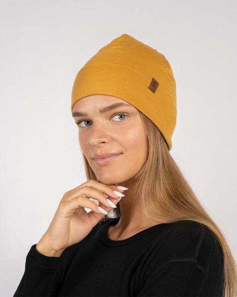 Close-up side view of woman in yellow merino beanie, touching her face gently.