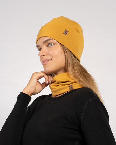 Woman in yellow Merino beanie and gaiter worn around neck, posing in black long sleeve top – side view.