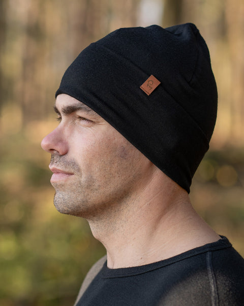 A man, standing outside during fall season, wearing the menique Men's Merino Beanie Hat in Black Color.