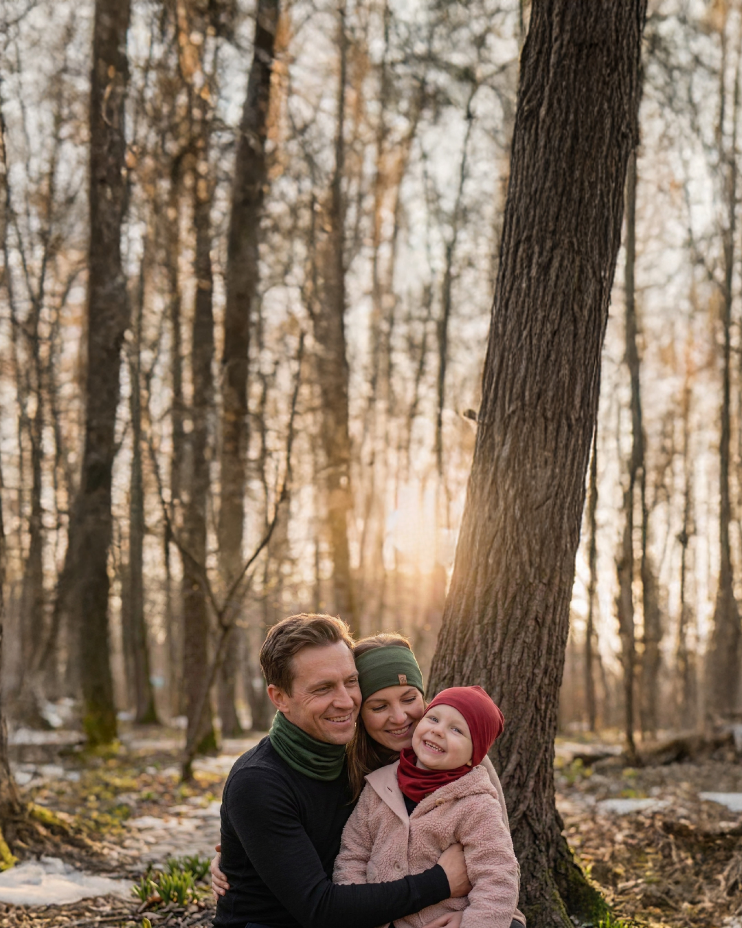 Family wearing merino wool accessories sitting together in a forest during cool weather.