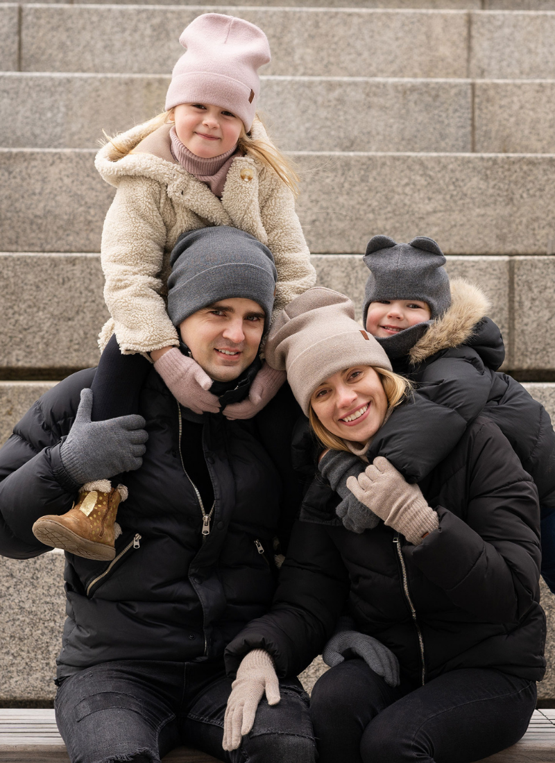Family dressed in winter jackets, merino wool hats, gloves, and scarves, sitting on stone steps outdoors in cold weather.