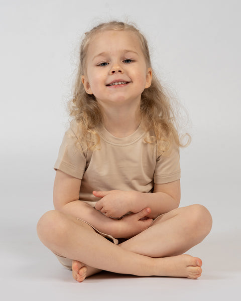 Child sitting cross-legged in beige bamboo t-shirt and shorts – soft comfortable kids outfit
