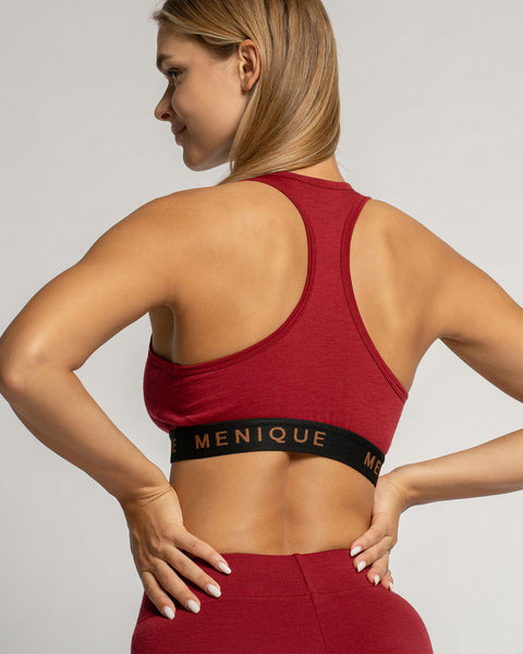 Woman wearing a red sports bra and leggings with 'Menique' branding on a light gray background