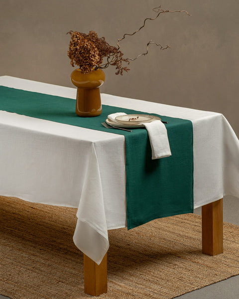 The dark green linen table runner on top of a wooden table, captured in a close up picture from the corner of the table. 