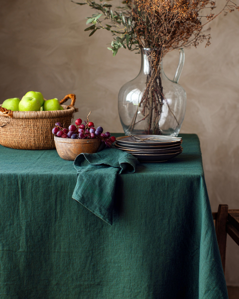 Dark green linen tablecloth styled with rustic fruit and woven basket décor on a dining table.