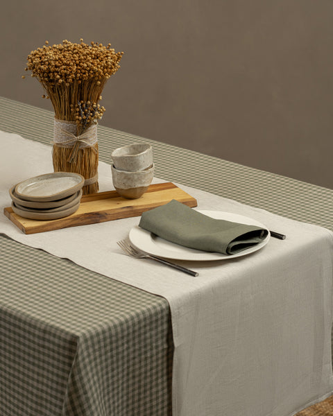 The menique natural linen table runner on top of a green check tablecloth. 