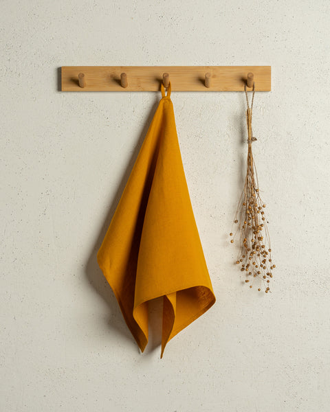 The menique linen kitchen dish towel in the color of spicy yellow hanging on a wooden rack on a wall.