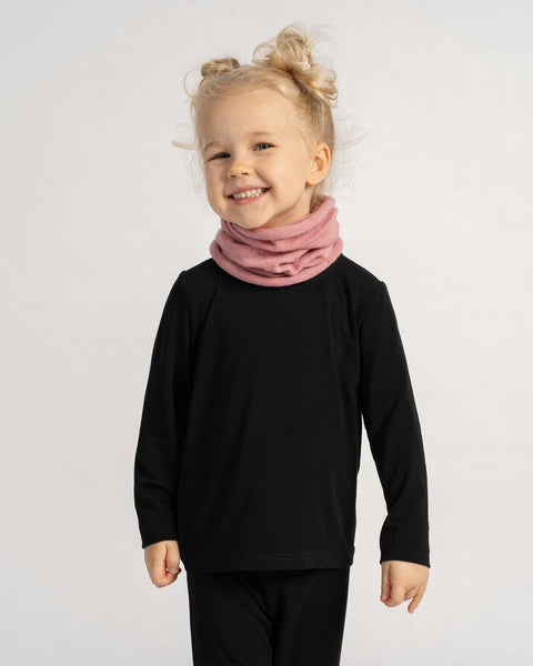 Smiling child in a black outfit wearing a soft pink knit neck warmer, posing cheerfully against a plain background.