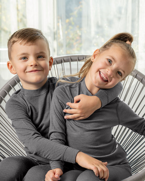 Happy boy and girl in gray Merino wool base layers sitting together in a chair, hugging and smiling.