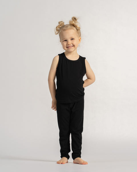 Child in a black sleeveless outfit standing barefoot against a light background.
