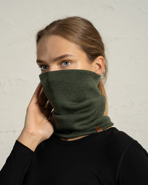 Woman wearing dark green knit Merino neck gaiter pulled over nose, cozy winter face and neck warmer.