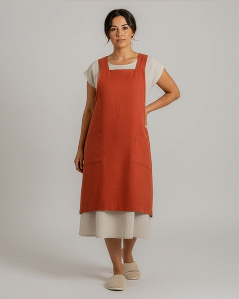 Woman wearing a cinnamon red apron over a white shirt on a plain background