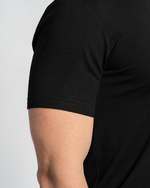 Close-up of a merino black t-shirt sleeve, showing the fabric texture and seam details. The t-shirt is displayed on a person's arm, with a light background.