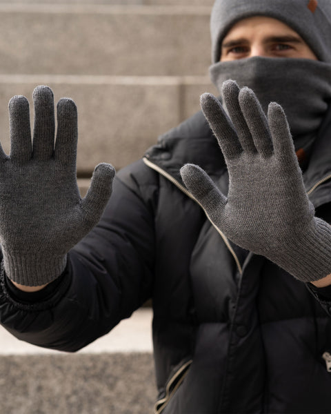 Man wearing dark gray Merino wool gloves and winter accessories, holding hands up to show glove fit outdoors.