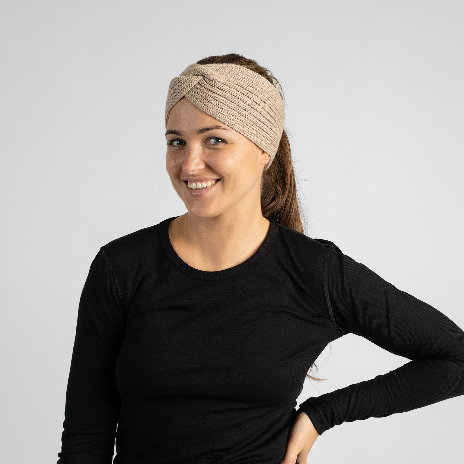 A chest-up studio portrait of a smiling woman wearing a black long-sleeve shirt and a dark brown knit headband.
