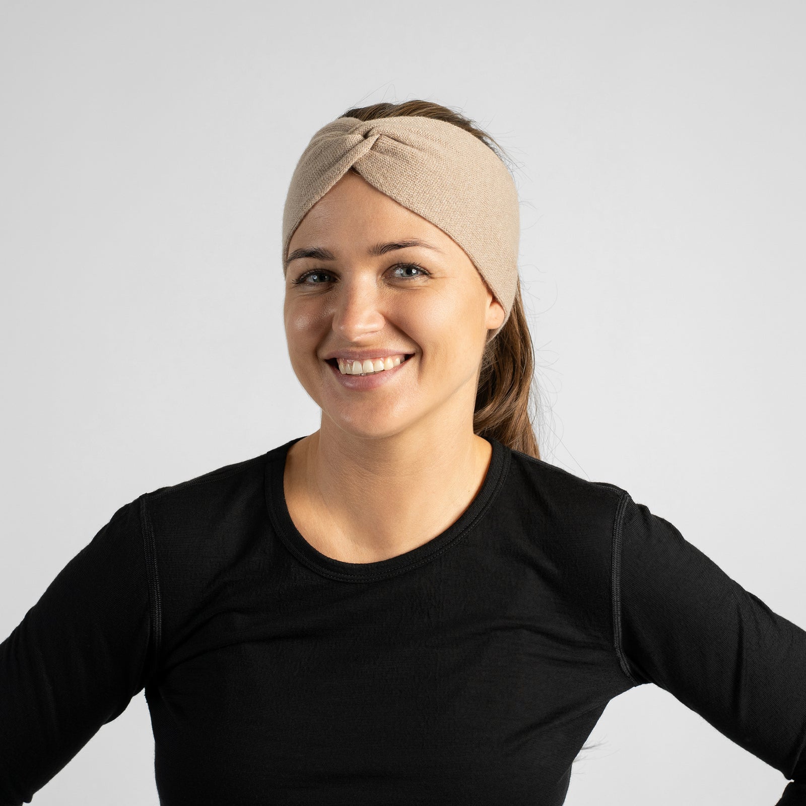 A smiling woman with her hair pulled back into a ponytail, wearing a dark gray or charcoal wide knit headband and a black long-sleeve top.