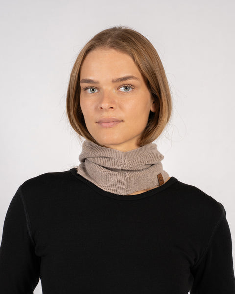Woman wearing a creamy beige knitted Merino wool balaclava styled as a neck warmer.
