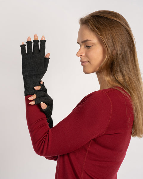 Side-profile of a woman in a red top wearing dark gray fingerless merino gloves, holding one wrist with the other hand.