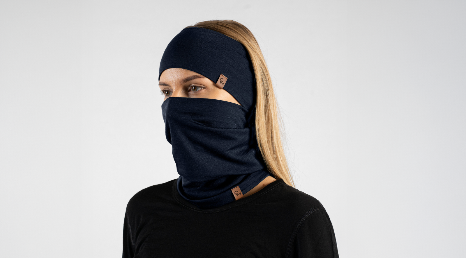 A woman wearing a dark navy blue full-head balaclava mask with a matching neck gaiter, shown from the chest up against a light gray studio background.