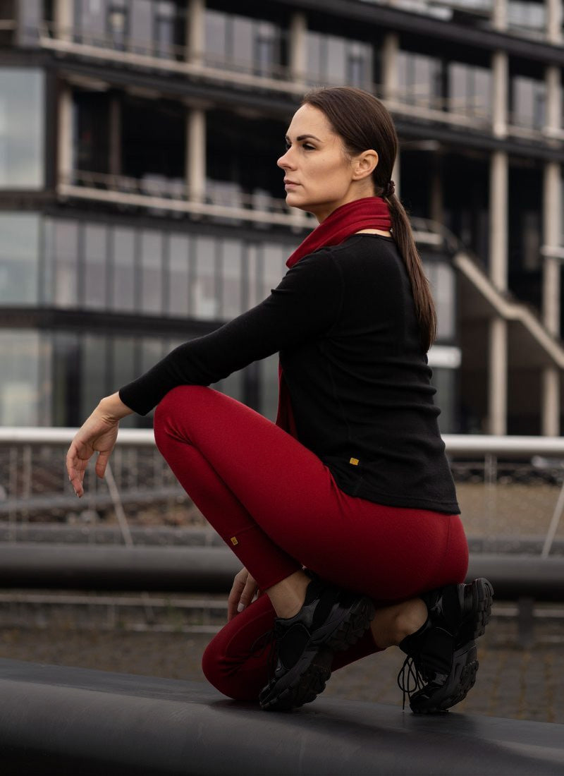 Woman in black top and red pants crouching in front of a modern building.